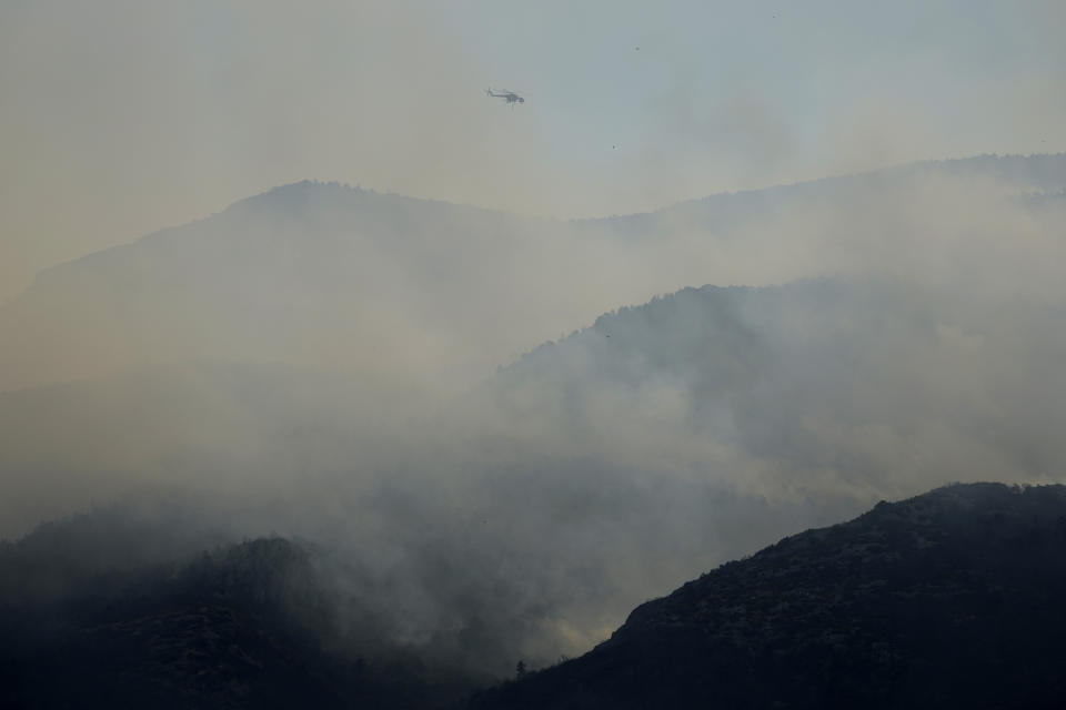A helicopter fly through smoke of a fire during a wildfire near Tatoi, in northern Athens, Greece, Saturday, Aug. 7, 2021. Wildfires rampaged through massive swathes of Greece's last remaining forests for yet another day Saturday, encroaching on inhabited areas and burning scores of homes, businesses and farmland. (AP Photo/Petros Karadjias)
