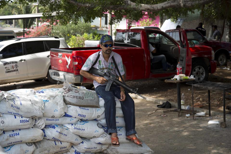 An armed man belonging to the Self-Defense Council of Michoacan (CAM) sits on sandbags at a checkpoint set up by the self-defense group in La Mira on the outskirts of the seaport of Lazaro Cardenas in western Mexico, Friday, May 9, 2014. Mexico’s government plans on Saturday to begin demobilizing the vigilante movement that largely expelled the Knights Templar cartel when state and local authorities couldn’t. But tension remained on Friday in the coastal part of the state outside the port of Lazaro Cardenas, where some self-defense groups plan to continue as they are, defending their territory without registering their arms. (AP Photo/Eduardo Verdugo)