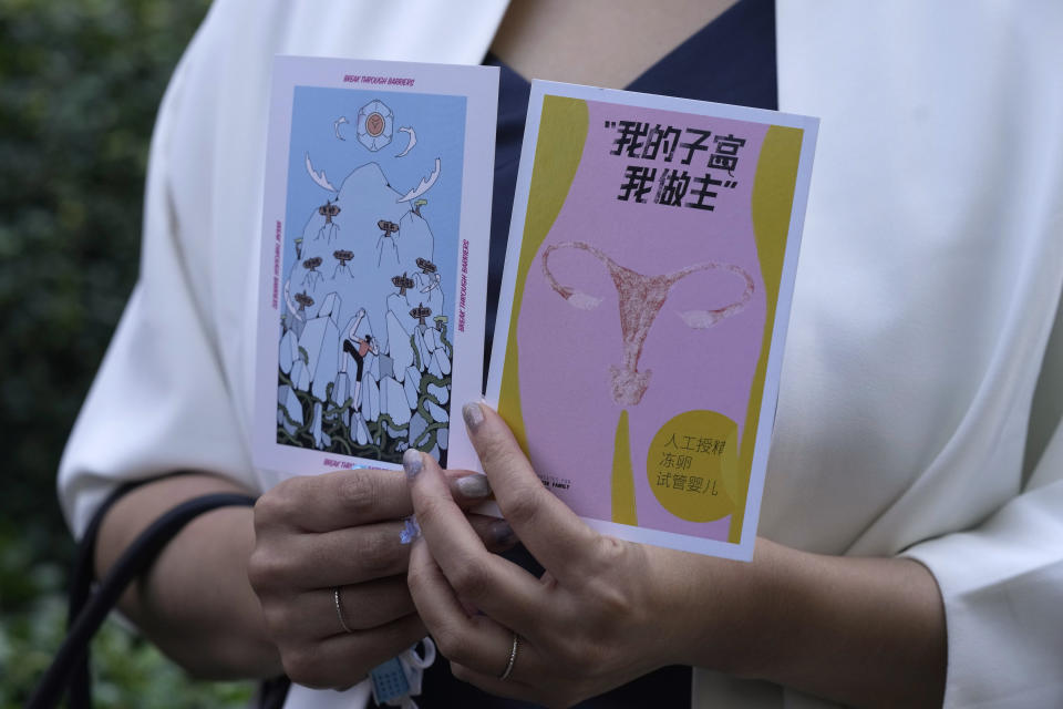 Teresa Xu holds up cards one of which reads "My Womb, My Choice" before attending a court session at the Chaoyang People's Court in Beijing, China, Friday, Sept. 17, 2021. After almost two years, the unmarried woman suing for the right to freeze her eggs in Beijing, is getting her case heard in court in the first legal challenge of its kind in China. (AP Photo/Ng Han Guan)