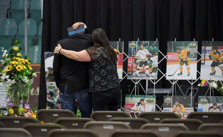 A man is comforted as he looks at photographs before a vigil at the Elgar Petersen Arena, home of the Humboldt Broncos, to honour the victims of a fatal bus accident in Humboldt, Saskatchewan, April 8, 2018. Jonathan Hayward/Pool via REUTERS