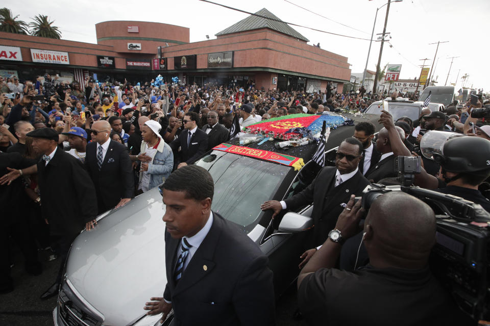 People watch as a hearse carrying the casket of slain rapper Nipsey Hussle passes Hussle's clothing store The Marathon, Thursday, April 11, 2019, in Los Angeles. Hussle’s casket, draped in the flag of his father’s native country, Eritrea in East Africa, embarked on a 25-mile tour of the city after his memorial service, drawing thousands to the streets to catch a glimpse of the recently-anointed hometown hero. (AP Photo/Jae C. Hong)