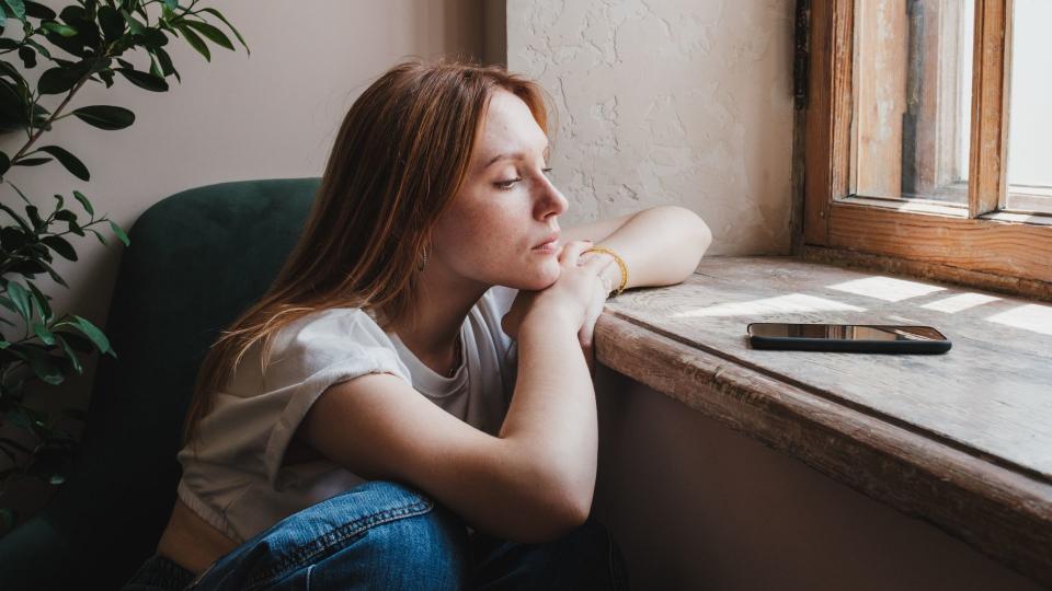 Woman leaning with head in her hands looking at phone on windowsill