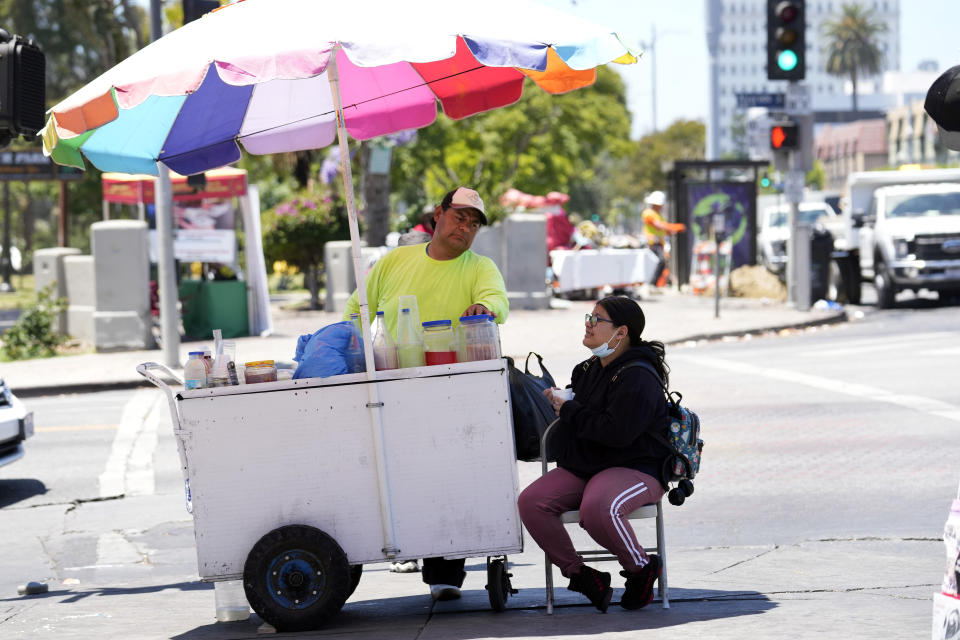 A street vendor selling snow cones tends to a customer at a street corner near MacArthur Park, Tuesday, July 11, 2023, in Los Angeles. (AP Photo/Marcio Jose Sanchez)