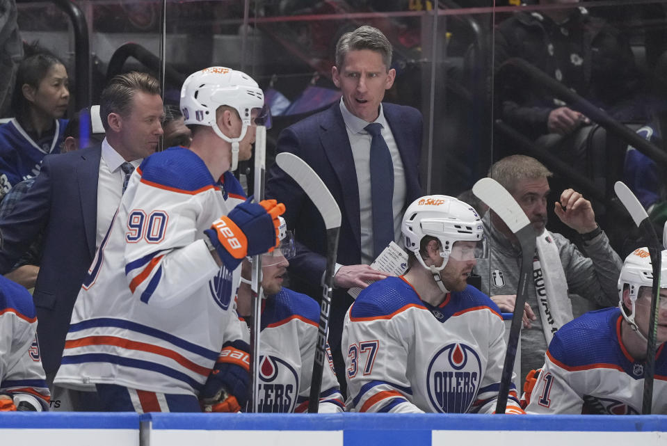 Edmonton Oilers coach Kris Knoblauch, center, talks to Corey Perry (90) during the first period of Game 1 of the team's second-round NHL hockey Stanley Cup playoffs series against the Vancouver Canucks, Wednesday, May 8, 2024, in Vancouver, British Columbia. (Darryl Dyck/The Canadian Press via AP)