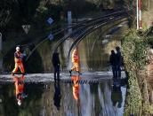 Railway workers are seen crossing the tracks after the river Thames flooded the railway in the village of Datchet, southern England February 10, 2014. REUTERS/Eddie Keogh