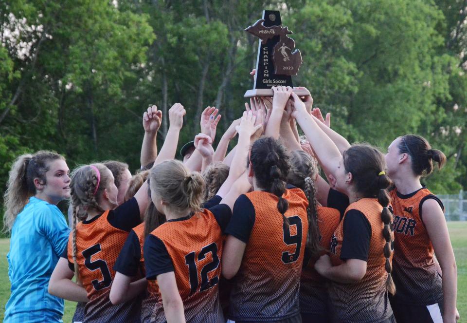 Harbor Springs players rush in to get a hand on the Division 4 district championship trophy Friday night at Ottawa Stadium in Harbor Springs after a 3-2 shootout victory over Charlevoix.