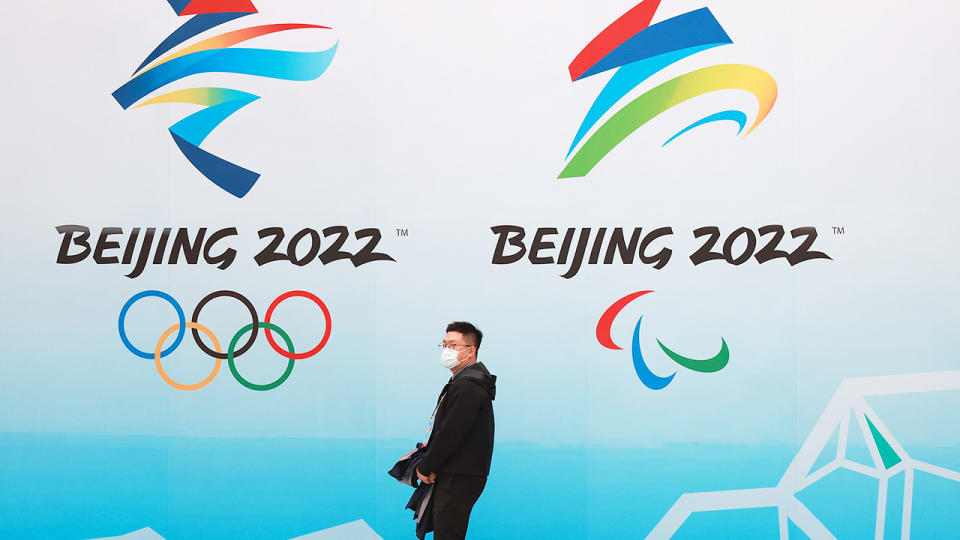 A man, pictured here wearing a protective mask as he walks in front the logos of the 2022 Beijing Winter Olympics.