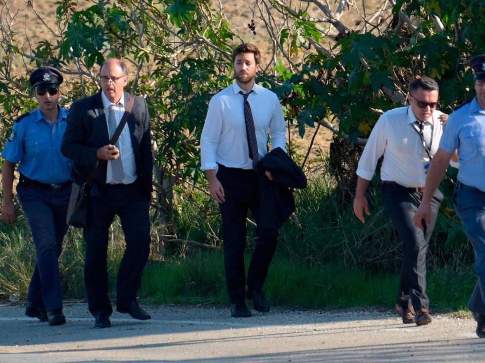 Matthew Caruana Galizia, middle, walks with policemen past the wreckage of a car bomb that killed Daphne Caruana Galizia close to her home in Bidnija, Malta (AFP)