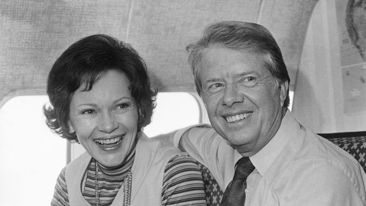 jimmy carter and rosalynn carter smile and look past the camera while sitting on an airplace