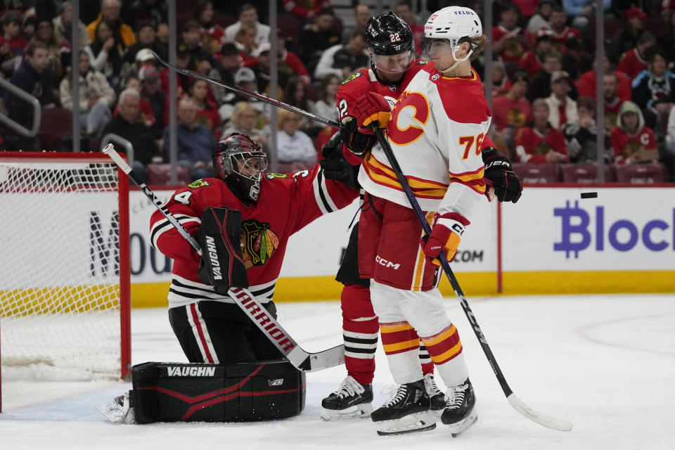 Calgary Flames center Martin Pospisil (76) is hit with the puck in front of the goal with Chicago Blackhawks goaltender Petr Mrazek and defenseman Nikita Zaitsev looking on during the second period of an NHL hockey game Sunday, Jan. 7, 2024, in Chicago. (AP Photo/Erin Hooley)