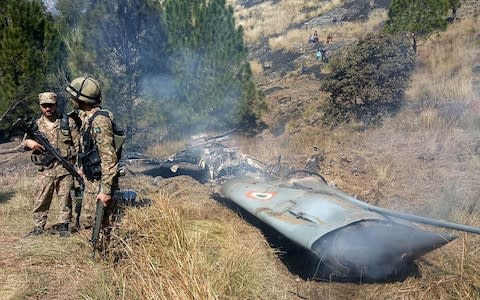 Pakistani soldiers stand next to what Pakistan says is the wreckage of an Indian fighter jet shot down in Pakistan controled Kashmir at Somani area in Bhimbar district - Credit: AFP