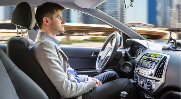 Photo of a man sitting in a self-driving vehicle on a city street.