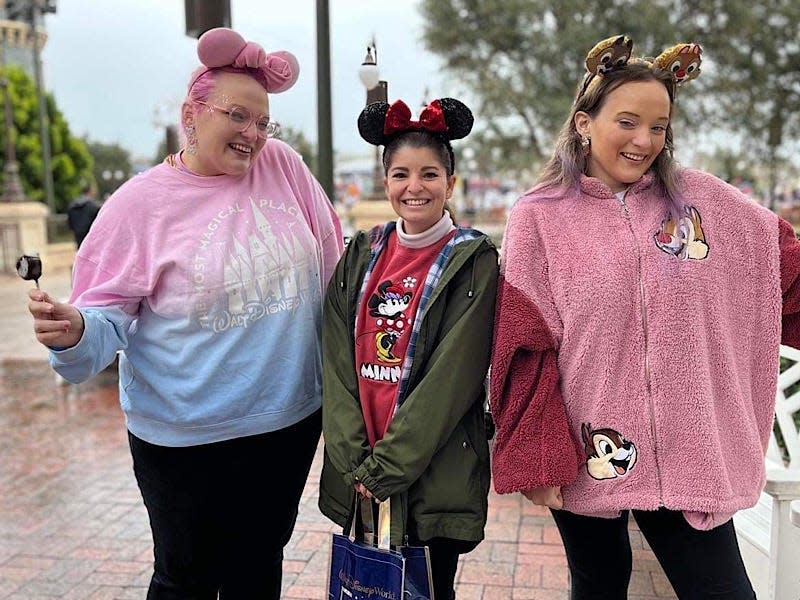 Three girls, including the writer, wear mouse ears and smile for the camera. The girl on the left wears a pink and blue sweatshirt with a castle on it, the girl in the middle wears a green jacket and red sweatshirt, and the writer, on the right, wears a pink fleece hoodie with Chip and Dale on it