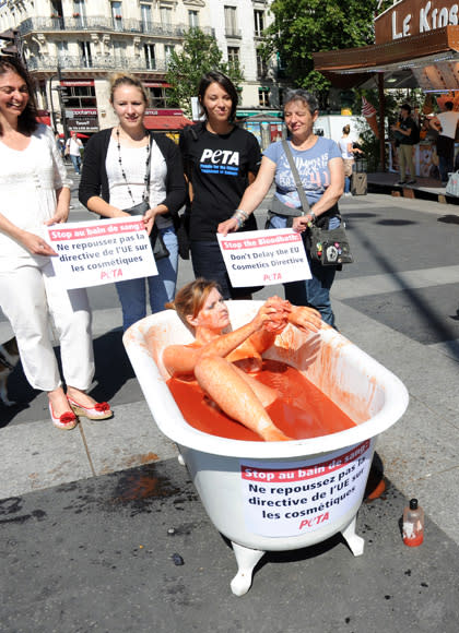 An activist from the association "People for the Ethical Treatment of Animals" (PETA) bathes in a bathtub fed up with tomato sauce "to symbolise a bloodshed",as pedestrians look on, on August 8, 2012, at the Bastille square in Paris, to denounce (boards at second ground) a European Union project. The European Commission plans to push to the end of 2013 the ban on the cosmetic industry to use in their products ingredients tested on animals. AFP PHOTO MEHDI FEDOUACH