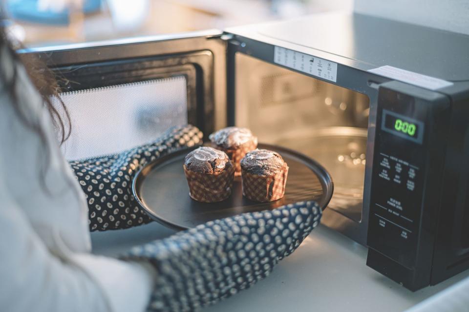 an asian chinese female putting cakes on a plate to microwave to heat up wearing kitchen glove