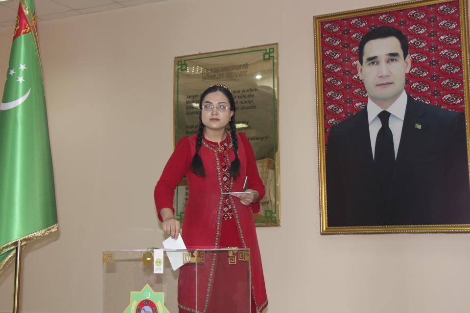 A woman wearing a national costume casts her ballot at a polling station with a portrait of President Serdar Berdymukhamedov, who was elected last year to succeed his father who had run the isolated ex-Soviet country for more than a decade in Ashgabat, Turkmenistan, Sunday, March 26, 2023. Voters in Turkmenistan have cast ballots for a new parliament that is expected to be opposition-free and loyal to the government of the gas-rich Central Asian nation. Sunday's election for 125 members included 258 candidates, put forward by three political parties or running independently. (AP Photo/Alexander Vershinin)