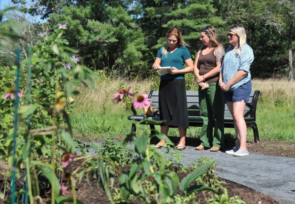 Meghan Bates, left, a daughter of Nancy Hemingway, reads a poem during the dedication of a memorial garden honoring the late Norwell conservation agent. With Bates are her sisters Niki Wix, center, and Danielle Kogut.