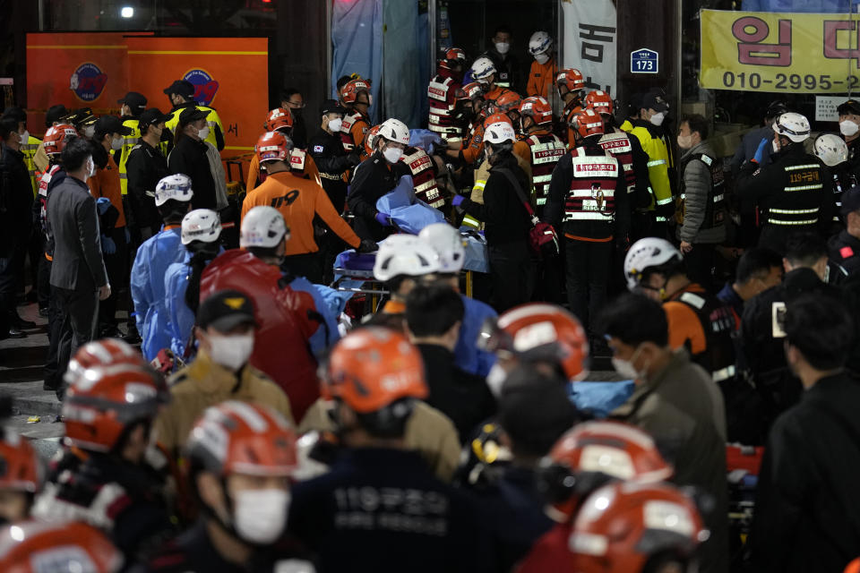 Rescue workers try to carry victims near the scene where scores of people died and were injured in Seoul, South Korea, Sunday, Oct. 30, 2022. Witnesses say the nightmarish scene intensified as people performed CPR on the dying and carried limp bodies to ambulances, while dance music pulsed from garish clubs lit in bright neon. Others tried desperately to pull out those who were trapped underneath the crush of people, but failed because too many in the crowd had fallen on top of them. (AP Photo/Lee Jin-man)