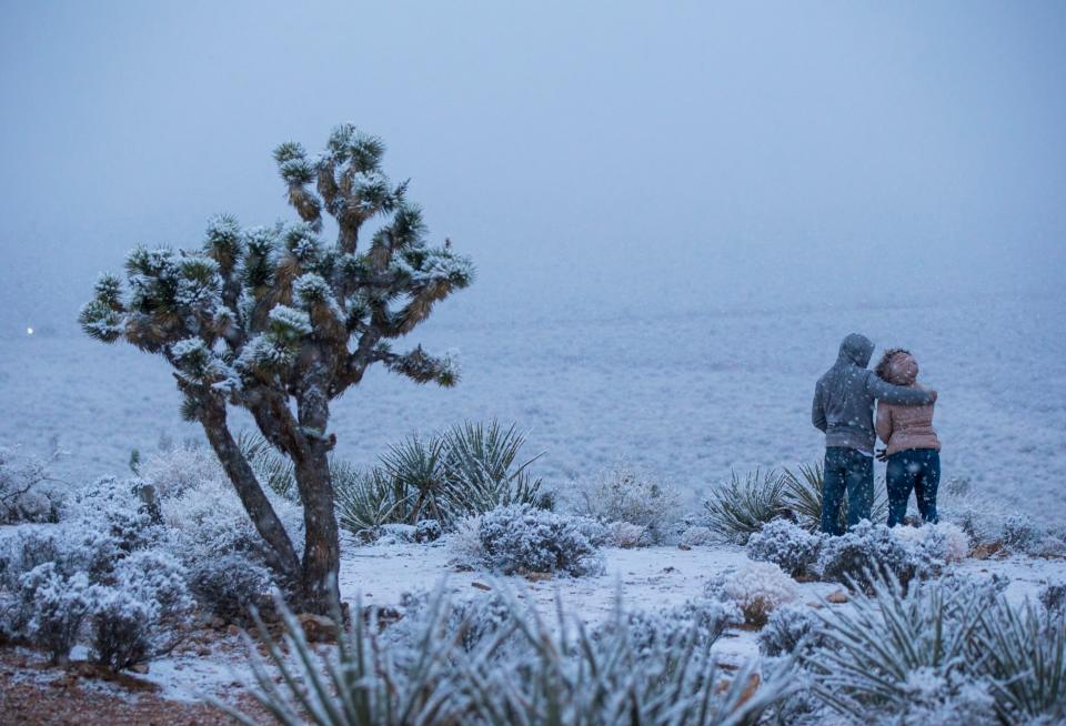 James Minner, of Las Vegas, left, and Candace Reid, of Albuquerque, N.M., watch as snow falls around the overlook at the Red Rock Canyon National Conservation Area (AP)