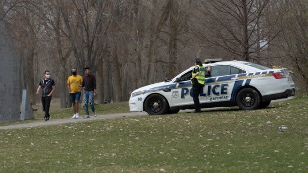 A Gatineau Police Service officer stands watch at Parc des Cèdres in the city's Aylmer district as three men walk by on April 11, 2021.