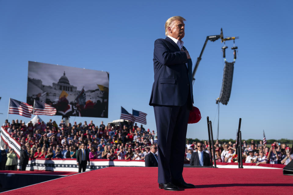 FILE - As footage from the Jan. 6, 2021, insurrection at the U.S. Capitol is displayed in the background, former President Donald Trump stands while a song, "Justice for All," is played during a campaign rally at Waco Regional Airport, March 25, 2023, in Waco, Texas. A lawyer for Trump said Thursday, March 30, that he has been told that the former president has been indicted in New York on charges involving payments made during the 2016 presidential campaign to silence claims of an extramarital sexual encounter. (AP Photo/Evan Vucci, File)