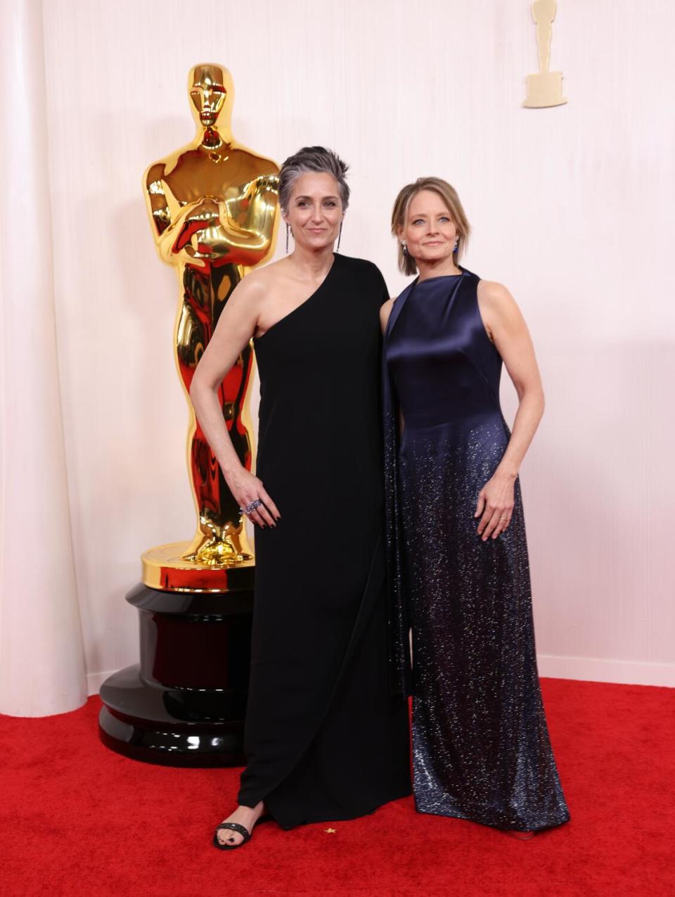 Alexandra Hedison, in a black one-shoulder gown, and Jodie Foster, in a navy blue gown, pose for cameras.