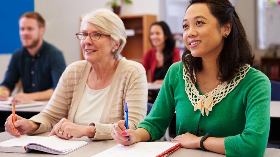 Two women sharing a desk at an adult education class look up.