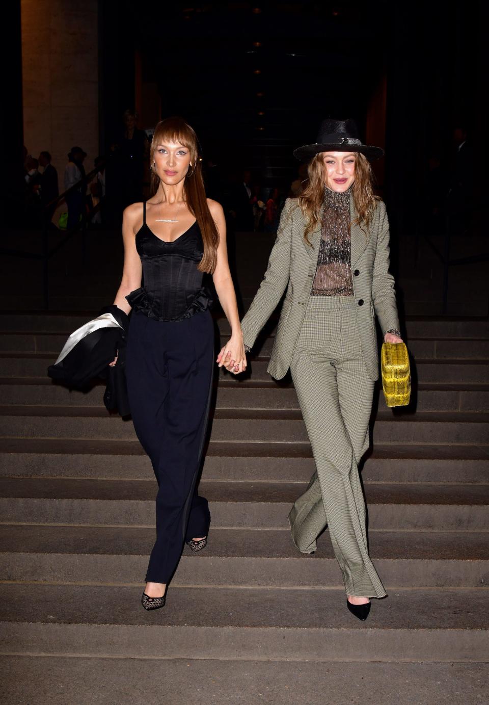 Bella and Gigi Hadid hold hands and walk down a staircase.