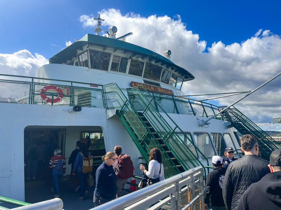 A white ferry with a sign that says "Walla Walla" with a green railing and staircase and passengers boarding