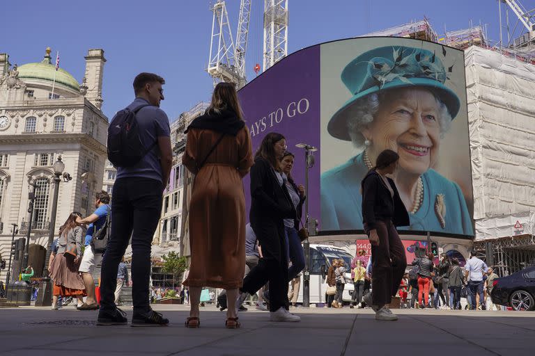 La gente pasa frente a la pantalla en Piccadilly Circus mientras muestra una cuenta regresiva de 7 días para el Jubileo de Platino de la reina, con dos fotos de Isabel de Gran Bretaña, en Londres, el viernes 27 de mayo de 2022.(AP Photo/Alberto Pezzali)