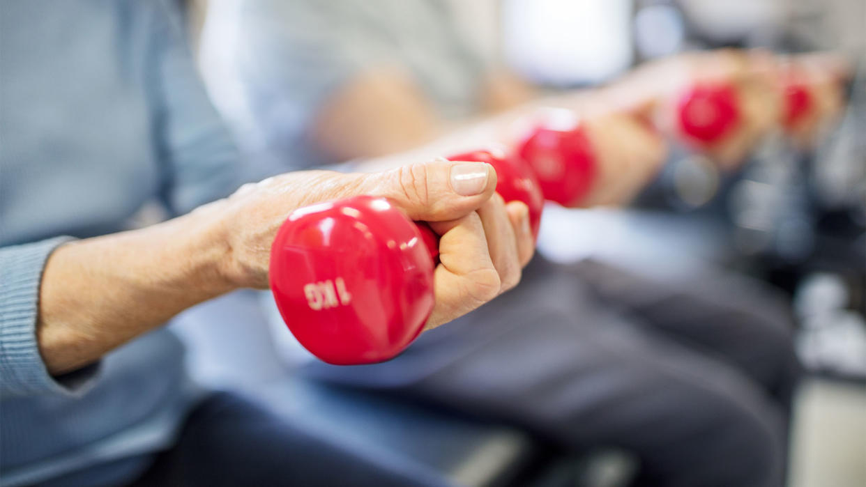  Close up on an older woman's hand as she lifts a small red dumbell in a gym. 