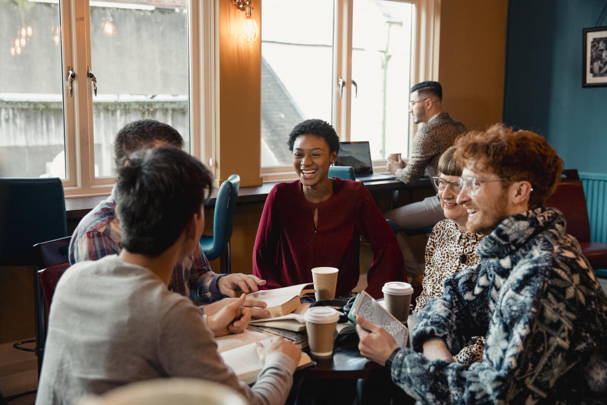 Small group of people with a mixed age range talking and laughing while having a book club meeting.