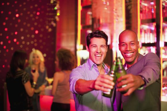 Two young men cheers beer bottles at a bar.