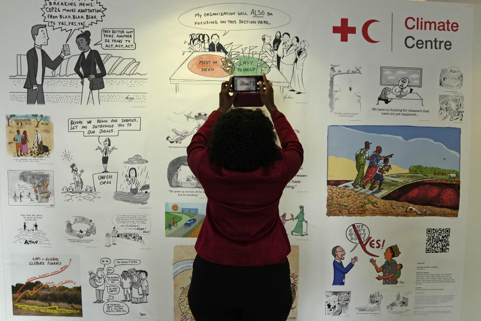 A woman takes photos of climate change cartoons at the COP26 U.N. Climate Summit in Glasgow, Scotland, Sunday, Oct. 31, 2021. The U.N. climate summit in Glasgow formally opens Sunday, a day before leaders from around the world gather in Scotland's biggest city to lay out their vision for addressing the common challenge of global warming. (AP Photo/Alastair Grant)