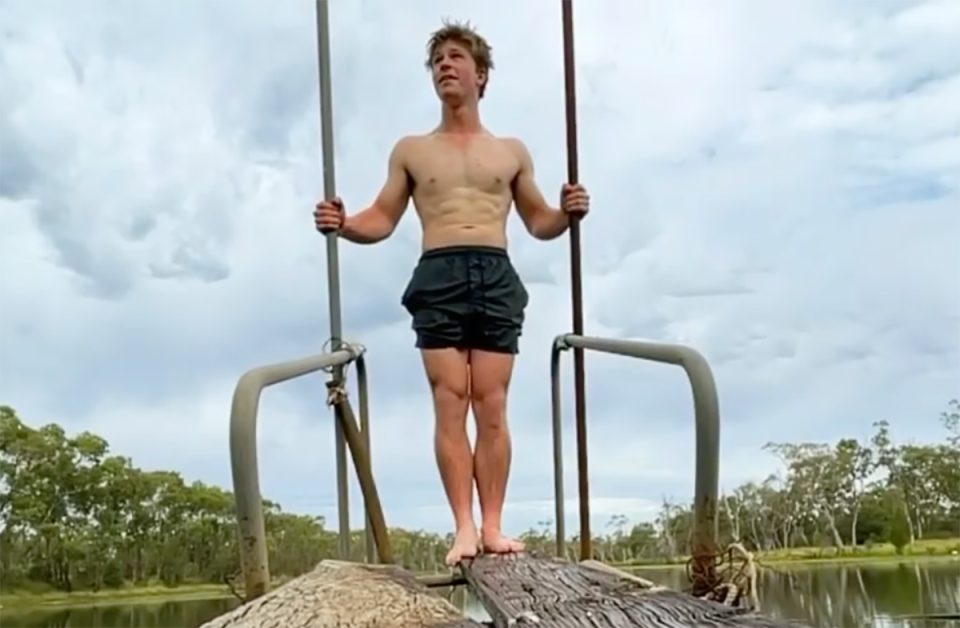 Robert Irwin standing shirtless on the edge of a wooden plank.