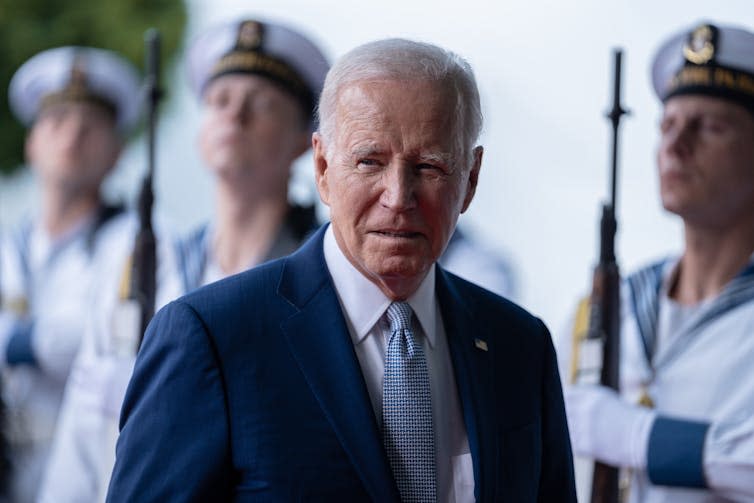 Joe Biden standing in front of navy servicemen holding guns.