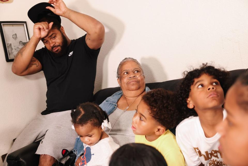 A man sits on the arm of a couch next to a woman and several young children