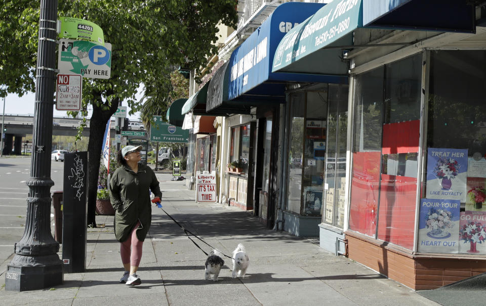 A woman looks at closed businesses as she walks her dog on Tuesday, March 17, 2020, in Oakland, Calif. Officials in seven San Francisco Bay Area counties have issued a shelter-in-place mandate affecting about 7 million people, including the city of San Francisco itself. The order says residents must stay inside and venture out only for necessities for three weeks starting Tuesday. (AP Photo/Ben Margot)