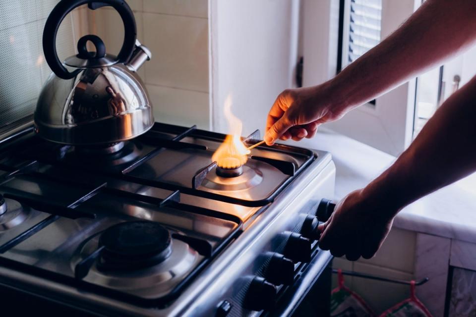 Person lighting gas burner on a stove with a match. A teapot is on the back burner.