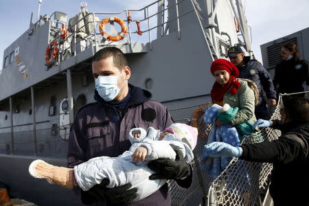 A Greek Coast Guard officer (L) carries a baby from the Ayios Efstratios Coast Guard vessel following a rescue operation at open sea, at the port of the Greek island of Lesbos, February 8, 2016. REUTERS/Giorgos Moutafis