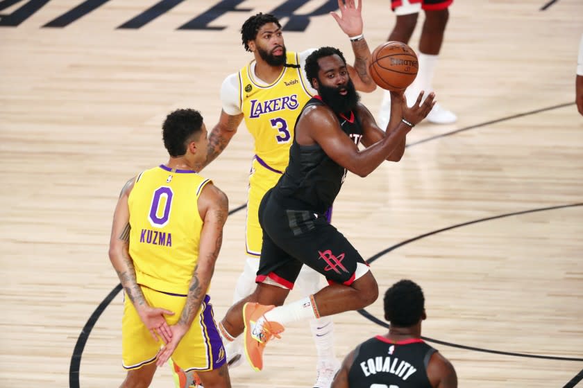 Rockets guard James Harden passes the ball between Lakers forward Kyle Kuzma and forward Anthony Davis.