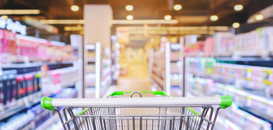 Empty shopping cart with supermarket aisle with cosmetic healthcare product shelves interior defocused blur background