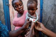 Cherlande Dolcine, 20, holds her daughter Dainaika Jean, 2, in front of their house as a measurement shows red for severe malnourishment in Port-de-Paix