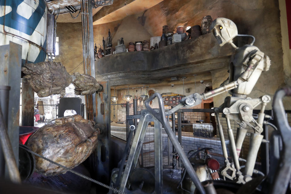 A robot cooks 'space meat' near the entrance of the Ronto Roasters restaurant during a preview of the Star Wars themed land, Galaxy's Edge in Hollywood Studios at Disney World, Tuesday, Aug. 27, 2019, in Lake Buena Vista, Fla. The attraction will open Thursday to park guests. (AP Photo/John Raoux)