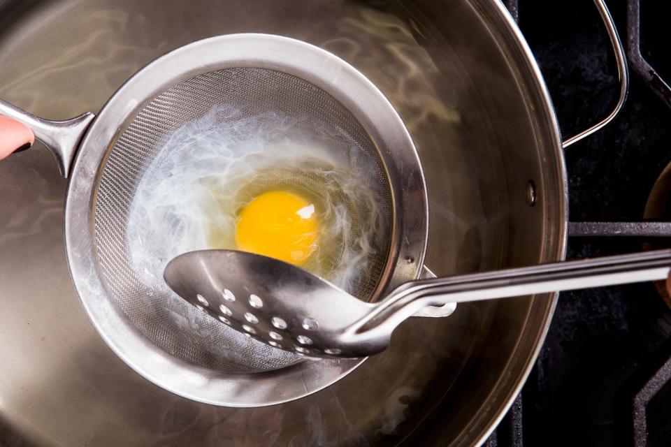 With the egg still in the strainer, carefully lower it into the hot water so that the egg is completely submerged. Gently shake and swirl the strainer and use a slotted spoon to shape the egg. When the edges of the egg white start to turn opaque (30 to 60 seconds), use the slotted spoon to carefully release it from the strainer into the water.