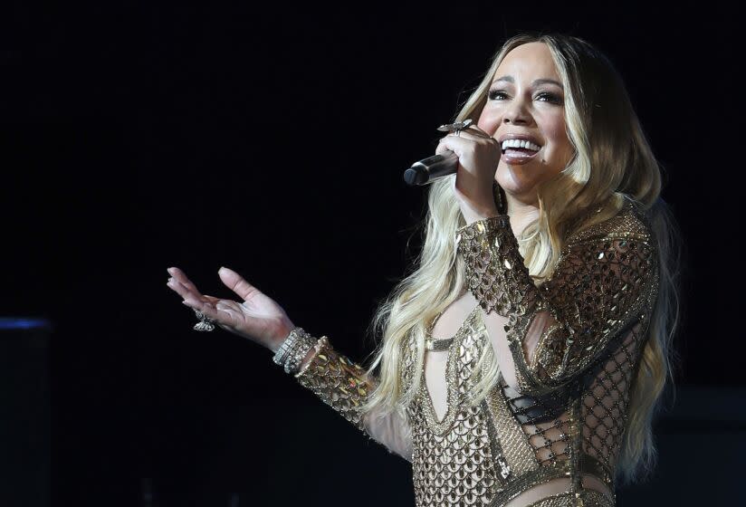 A woman with long hair gestures with one hand while singing into a microphone held in the other hand