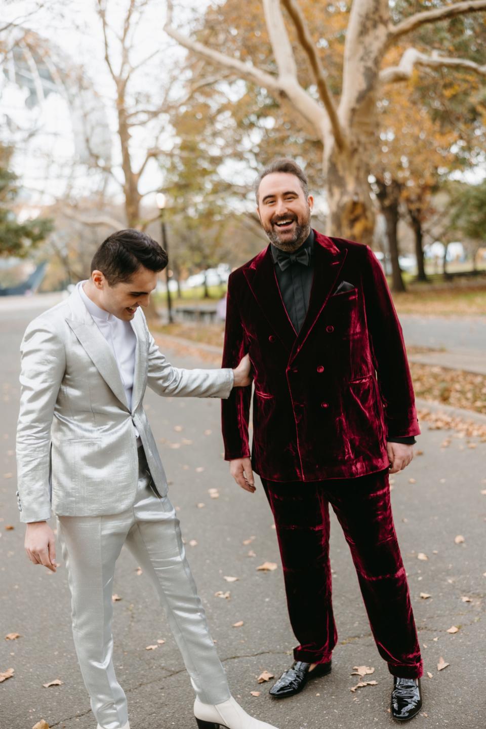 Two grooms in colorful suits stand in a park.