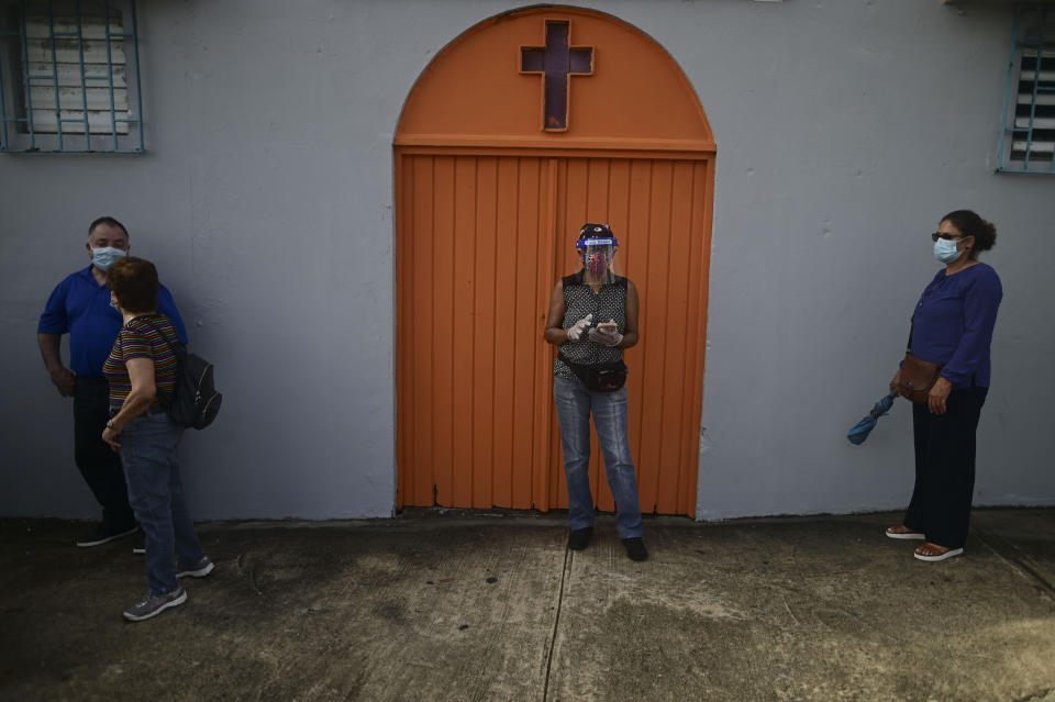 People practice social distancing amid the COVID-19 pandemic as they wait in line to vote for general elections, outside a church next door to the school serving as a voting center in San Juan, Puerto Rico, Tuesday, Nov. 3, 2020. In addition to electing a governor, Puerto Ricans are voting in a non-binding referendum on statehood. (AP Photo/Carlos Giusti)