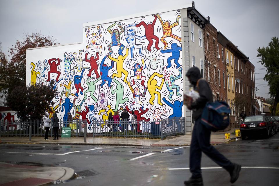 A postal worker walks past a 1987 mural titled "We The Youth" by artist Keith Haring Wednesday, Oct. 30, 2013, in the Point Breeze neighborhood of Philadelphia. The city’s Mural Arts Program has worked for months to restore the only collaborative public mural by Haring that is still intact and at its original site. Haring died of AIDS in 1990 at the age of 31. (AP Photo/Matt Rourke)