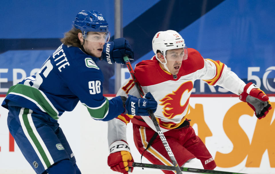 Vancouver Canucks center Adam Gaudette (96) and Calgary Flames center Mikael Backlund (11) watch the puck during the first period of an NHL hockey game Thursday, Feb. 11, 2021, in Vancouver, British Columbia. (Jonathan Hayward/The Canadian Press via AP)